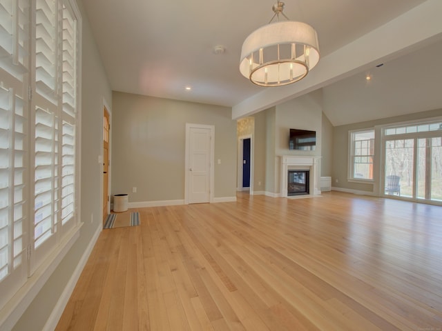 unfurnished living room with a glass covered fireplace, baseboards, light wood-type flooring, recessed lighting, and a chandelier