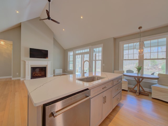 kitchen with a kitchen island with sink, stainless steel dishwasher, a sink, light wood-style floors, and white cabinetry