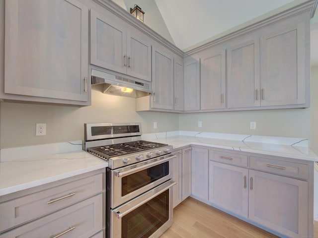 kitchen with light stone counters, range with two ovens, light wood-type flooring, under cabinet range hood, and gray cabinetry