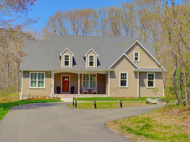 cape cod-style house with a shingled roof, covered porch, and a front yard