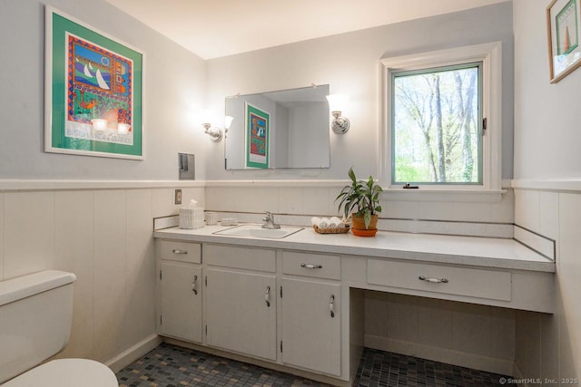 bathroom featuring a wainscoted wall, vanity, toilet, and a decorative wall