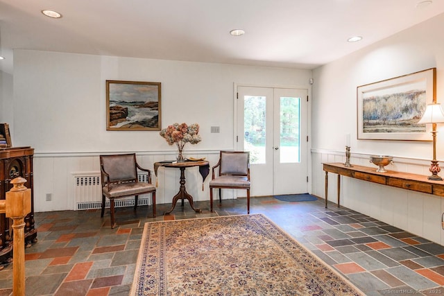 living area with radiator heating unit, a wainscoted wall, recessed lighting, and stone tile flooring