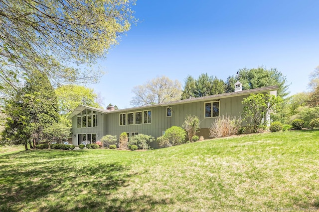 rear view of property with a lawn, board and batten siding, and a chimney