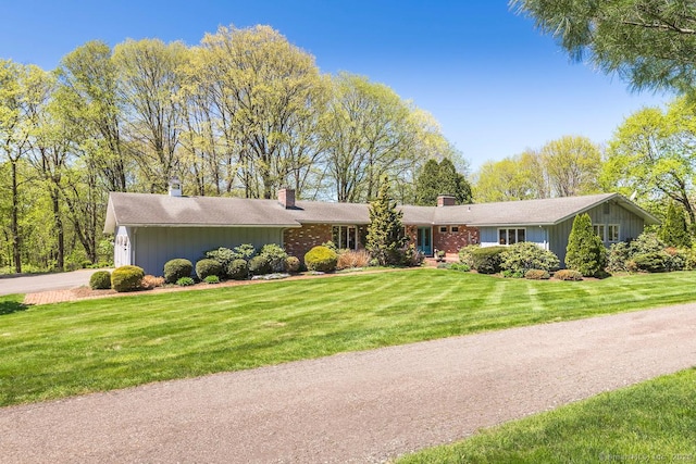 ranch-style home with an attached garage, a front lawn, driveway, and a chimney