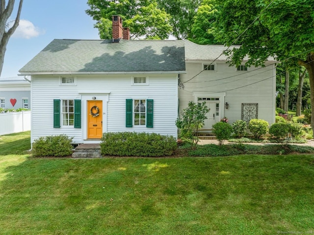 cape cod house featuring a front lawn, fence, roof with shingles, and a chimney