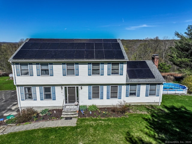 colonial inspired home with an outdoor pool, a front yard, a chimney, and solar panels