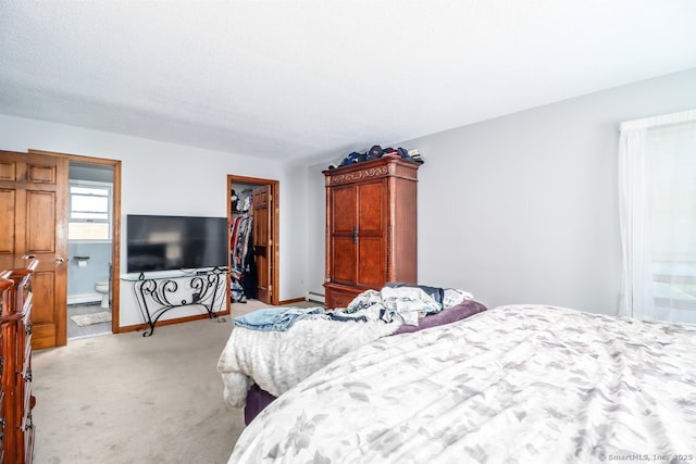 bedroom featuring light colored carpet, a walk in closet, baseboards, a baseboard radiator, and a closet