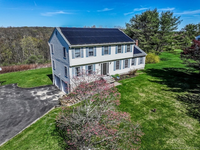 view of front of property featuring driveway, solar panels, a chimney, a front yard, and an attached garage
