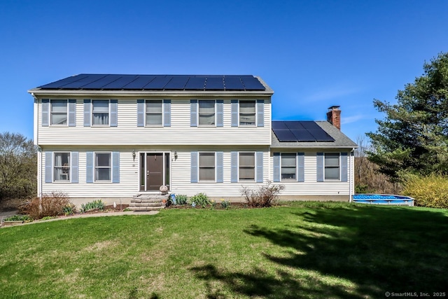 colonial house with a front yard, a chimney, a standing seam roof, metal roof, and solar panels