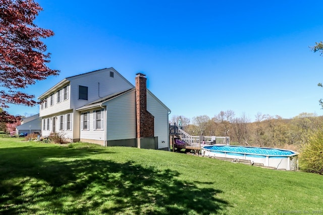 rear view of property with an outdoor pool, a yard, and a chimney