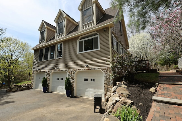 view of side of home featuring a garage, roof with shingles, driveway, and stone siding