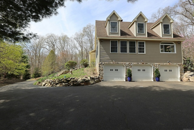 view of home's exterior with roof with shingles, an attached garage, driveway, and stone siding