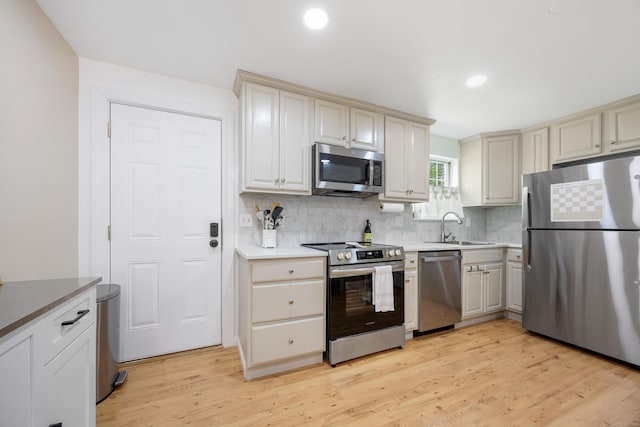 kitchen with appliances with stainless steel finishes, a sink, tasteful backsplash, light wood-style floors, and cream cabinets