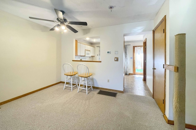 interior space featuring baseboards, ceiling fan, light carpet, and visible vents