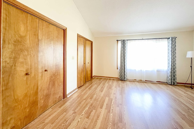 unfurnished bedroom with two closets, baseboards, vaulted ceiling, and light wood finished floors
