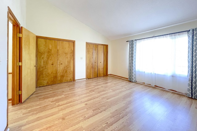 unfurnished bedroom with two closets, high vaulted ceiling, and light wood-style floors
