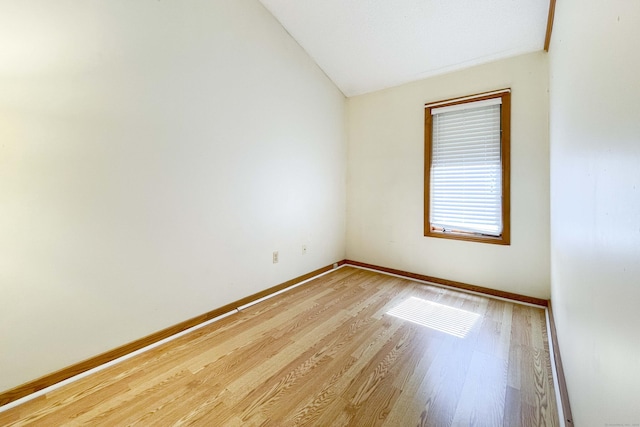 spare room featuring light wood-type flooring, baseboards, and vaulted ceiling