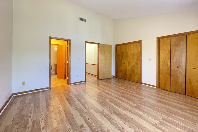 unfurnished bedroom featuring visible vents, a towering ceiling, two closets, baseboards, and light wood-style floors