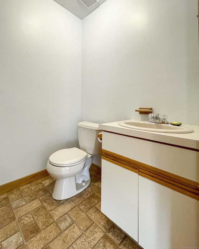 bathroom with vanity, stone tile floors, baseboards, and toilet