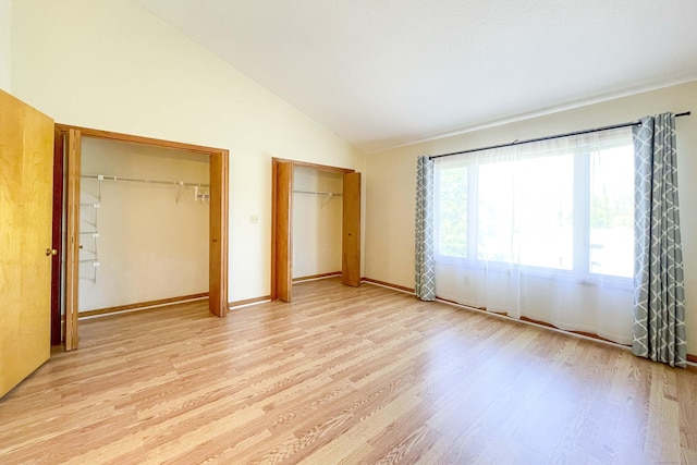 unfurnished bedroom featuring two closets, baseboards, vaulted ceiling, and light wood finished floors
