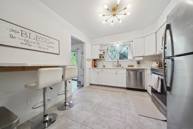 kitchen featuring decorative backsplash, light countertops, white cabinetry, a chandelier, and stainless steel appliances