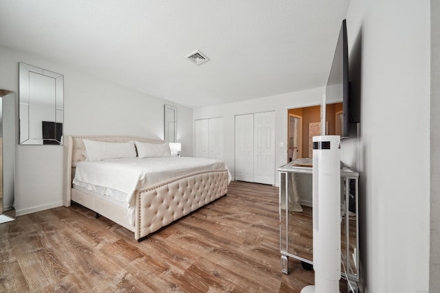 bedroom with two closets, wood finished floors, and visible vents