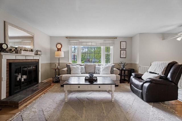 living room with wainscoting, ceiling fan, a fireplace, and wood finished floors