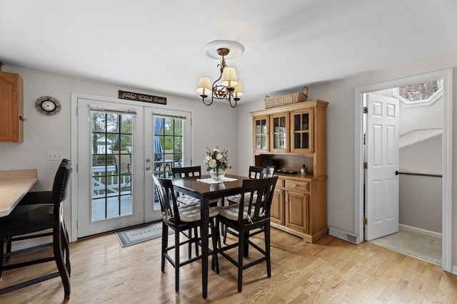 dining area with baseboards, light wood-style floors, an inviting chandelier, and french doors