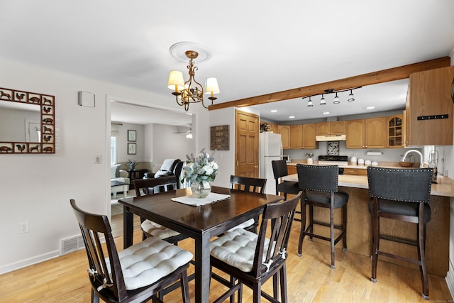dining space featuring light wood finished floors, rail lighting, a chandelier, and baseboards