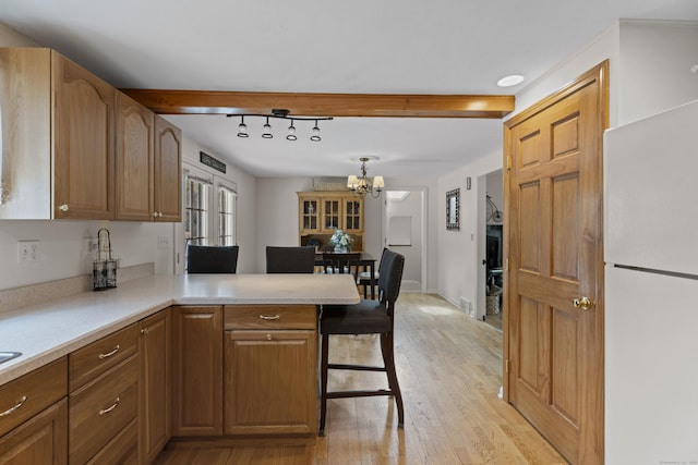 kitchen featuring a peninsula, an inviting chandelier, light wood-style flooring, freestanding refrigerator, and light countertops
