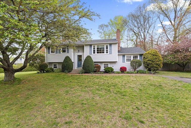raised ranch featuring a chimney, a front yard, and fence