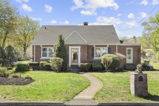 view of front of property with brick siding, a shingled roof, a front yard, and entry steps