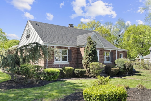 view of front of home with brick siding, a front lawn, roof with shingles, and a chimney