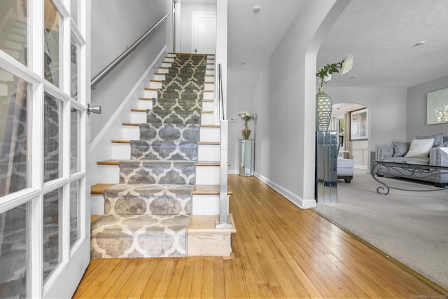 stairs with wood-type flooring, arched walkways, and baseboards
