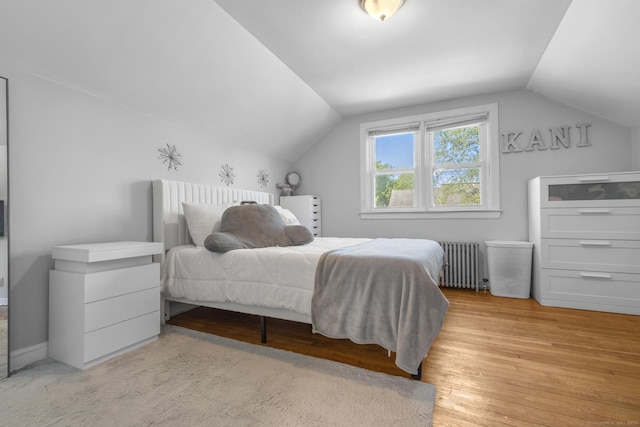 bedroom featuring radiator heating unit, lofted ceiling, and light wood-type flooring