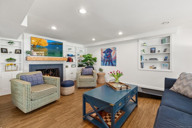 living room with built in shelves, wood finished floors, recessed lighting, and a tile fireplace