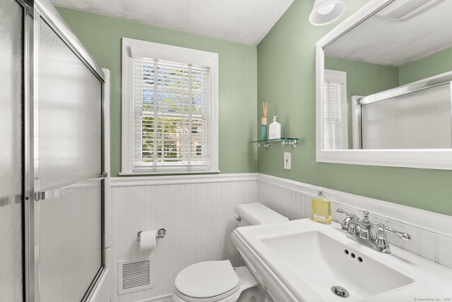 bathroom with toilet, a sink, a wainscoted wall, a shower with shower door, and visible vents