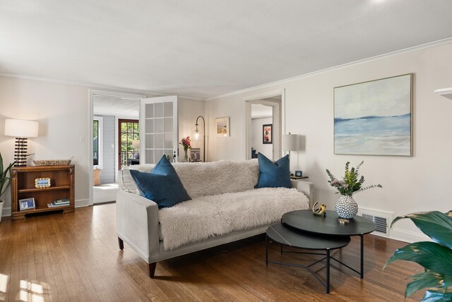 living area featuring visible vents, wood finished floors, baseboards, and ornamental molding
