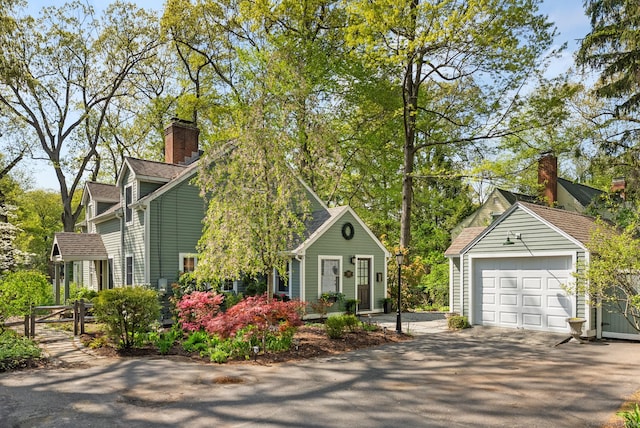view of front facade with an outbuilding, driveway, a detached garage, and a chimney