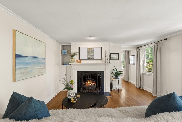 living room with a fireplace with flush hearth, crown molding, baseboards, and wood finished floors