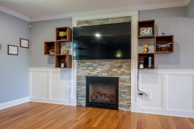 unfurnished living room with a glass covered fireplace, wood finished floors, crown molding, a decorative wall, and wainscoting