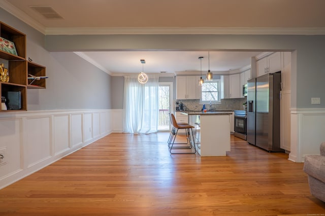 kitchen with stainless steel appliances, light wood-style flooring, a kitchen bar, crown molding, and a wainscoted wall