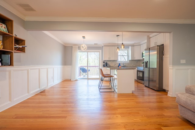 kitchen featuring appliances with stainless steel finishes, open floor plan, light wood-style floors, a kitchen breakfast bar, and a decorative wall