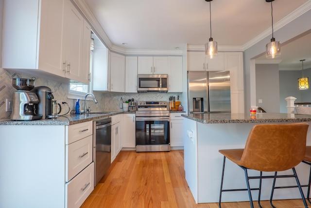 kitchen with stainless steel appliances, a sink, a breakfast bar, white cabinets, and ornamental molding