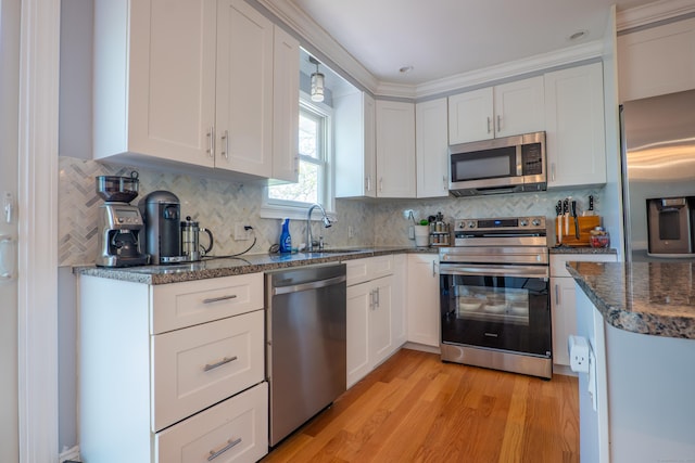 kitchen with appliances with stainless steel finishes, a sink, light wood-style flooring, white cabinets, and backsplash