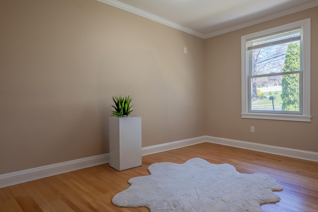 empty room featuring healthy amount of natural light, wood finished floors, baseboards, and crown molding