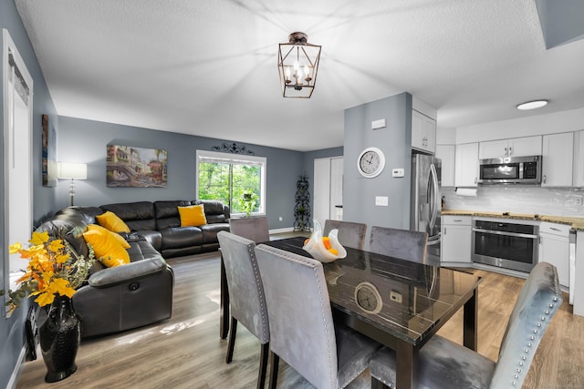 dining space featuring light wood finished floors, a chandelier, and a textured ceiling