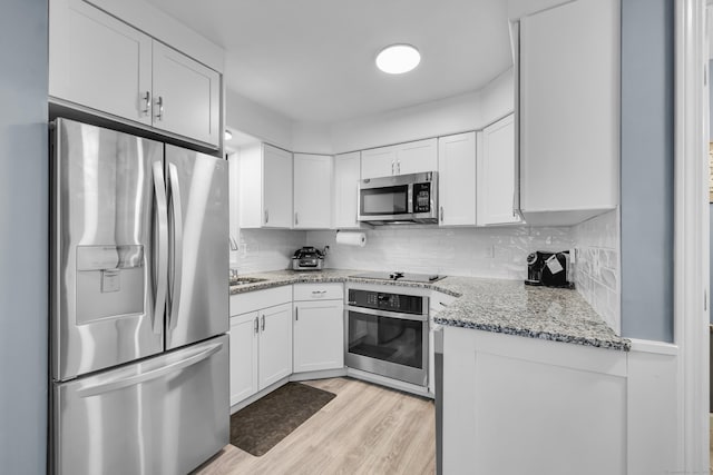 kitchen with appliances with stainless steel finishes, white cabinets, light wood finished floors, and decorative backsplash