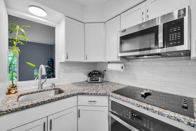 kitchen featuring stainless steel microwave, oven, a sink, and white cabinets