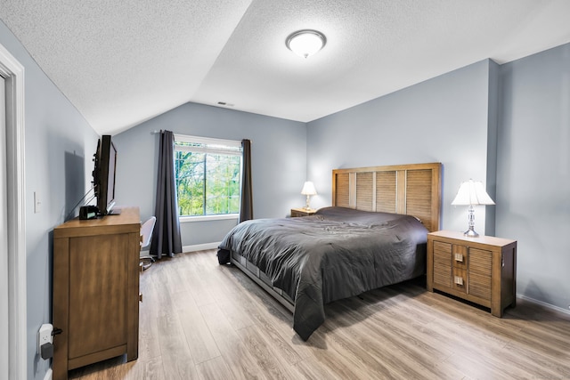 bedroom with light wood-type flooring, a textured ceiling, vaulted ceiling, and baseboards